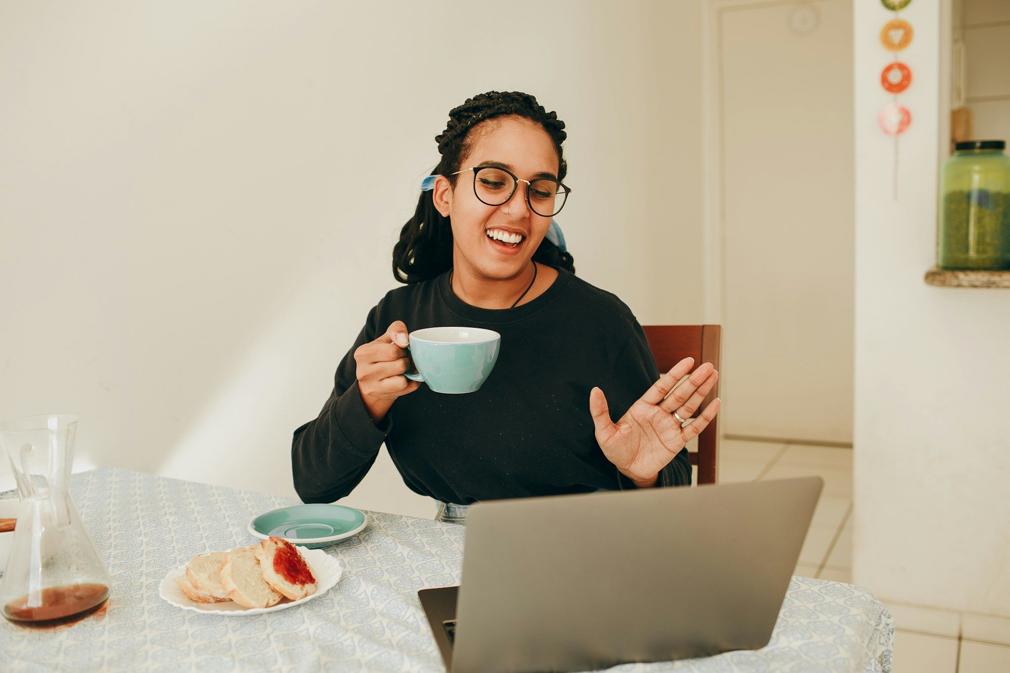 Mulher sorrindo em videochamada no notebook, segurando uma xícara na mesa de casa
