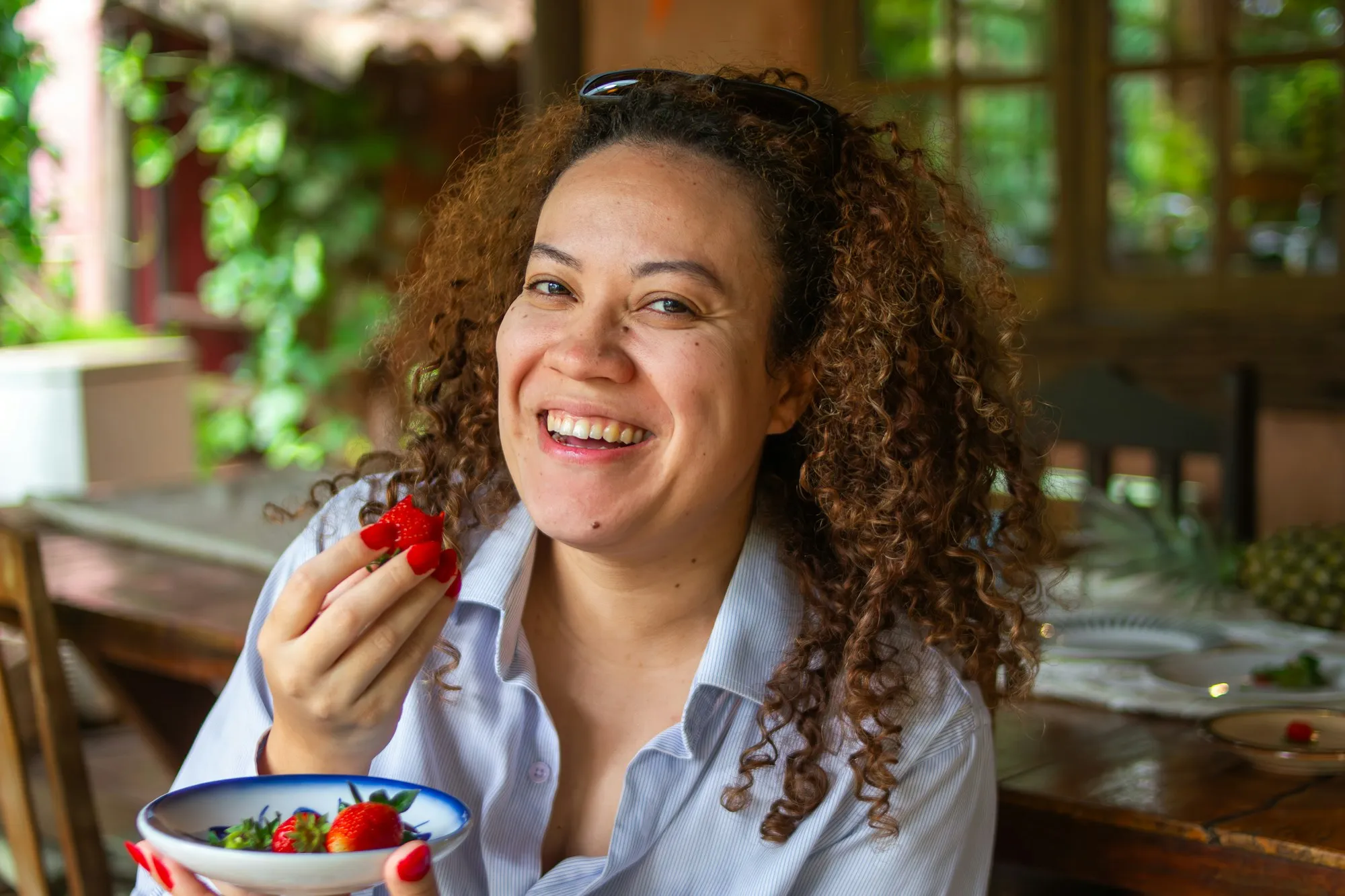 Mulher sorrindo enquanto come morangos em uma mesa ao ar livre