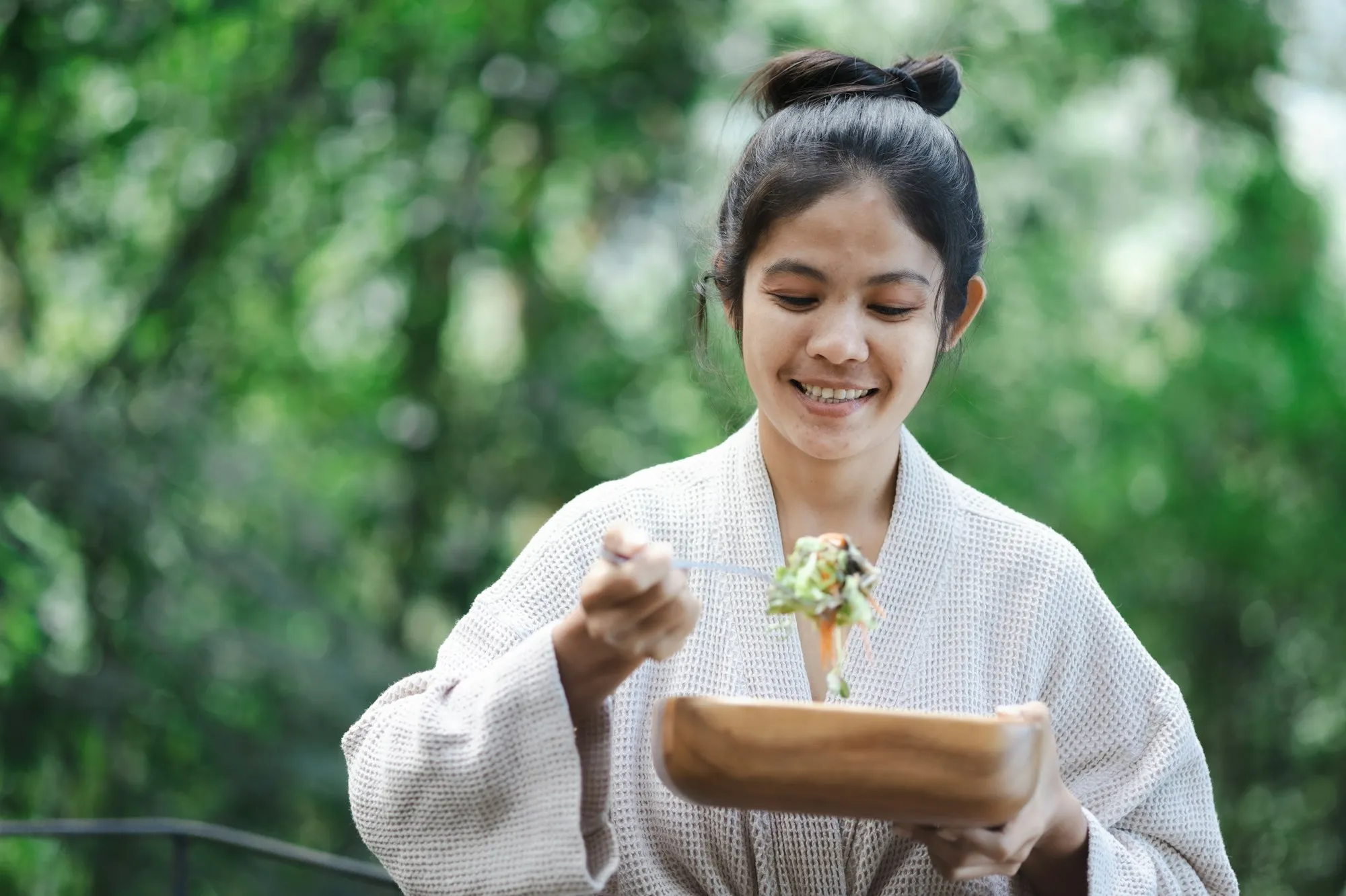 Mulher sorrindo ao comer salada em um jardim